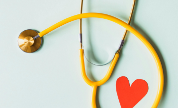 Medical stethoscope with red paper heart on white surface